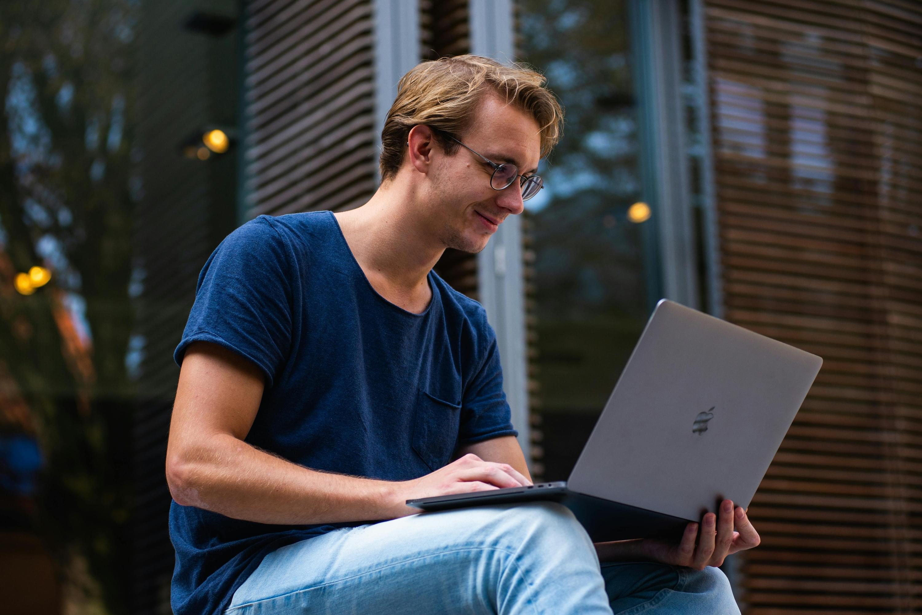 Junger Mann arbeitet entspannt mit Laptop im Außenbereich – Symbol für  ortsunabhängiges Arbeiten und flexible Vertriebsmodelle.