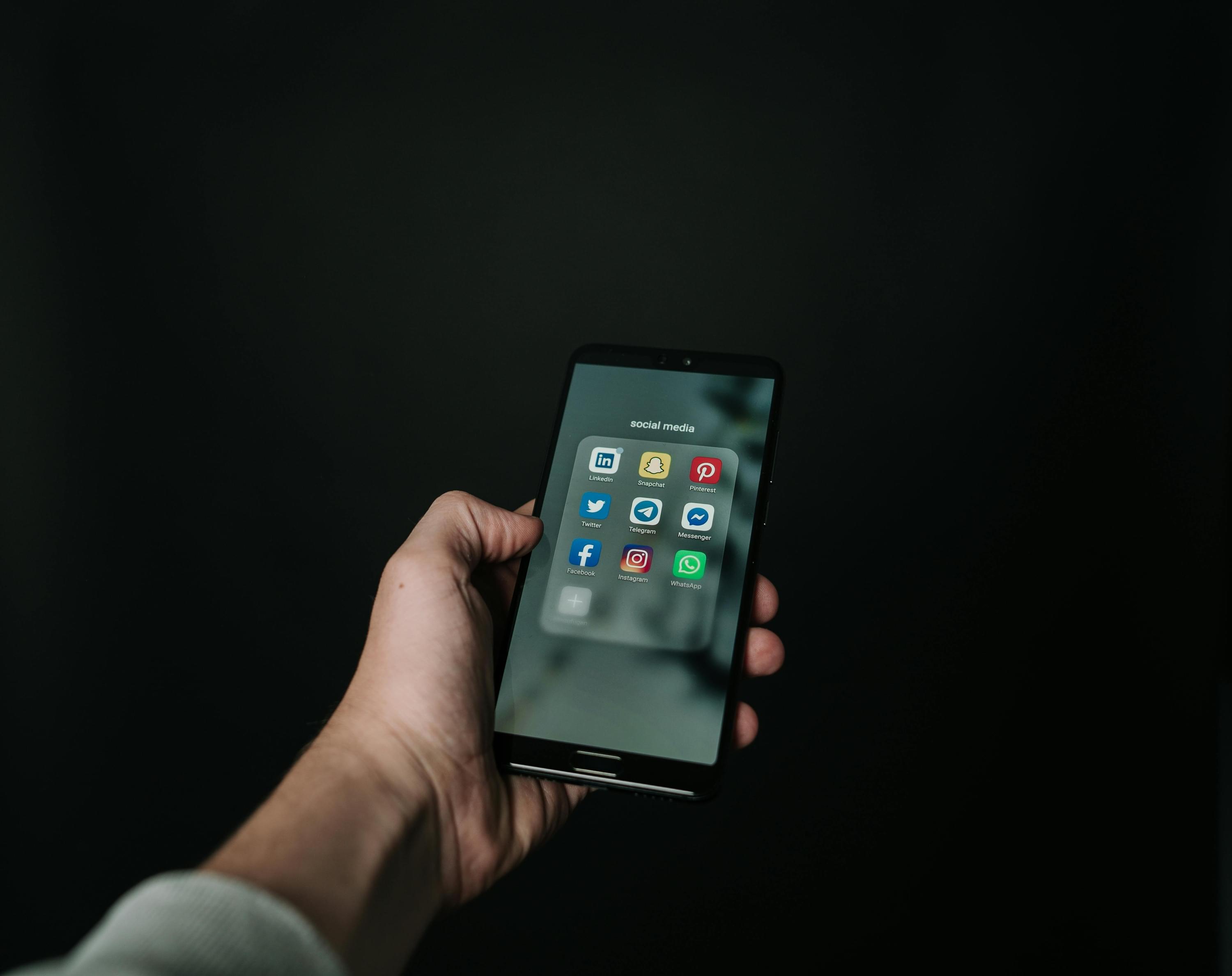 Eine Hand hält ein Smartphone mit geöffnetem Social-Media-Ordner – Symbol für  digitale Sichtbarkeit, Online-Präsenz und Plattformstrategie im Vertrieb.