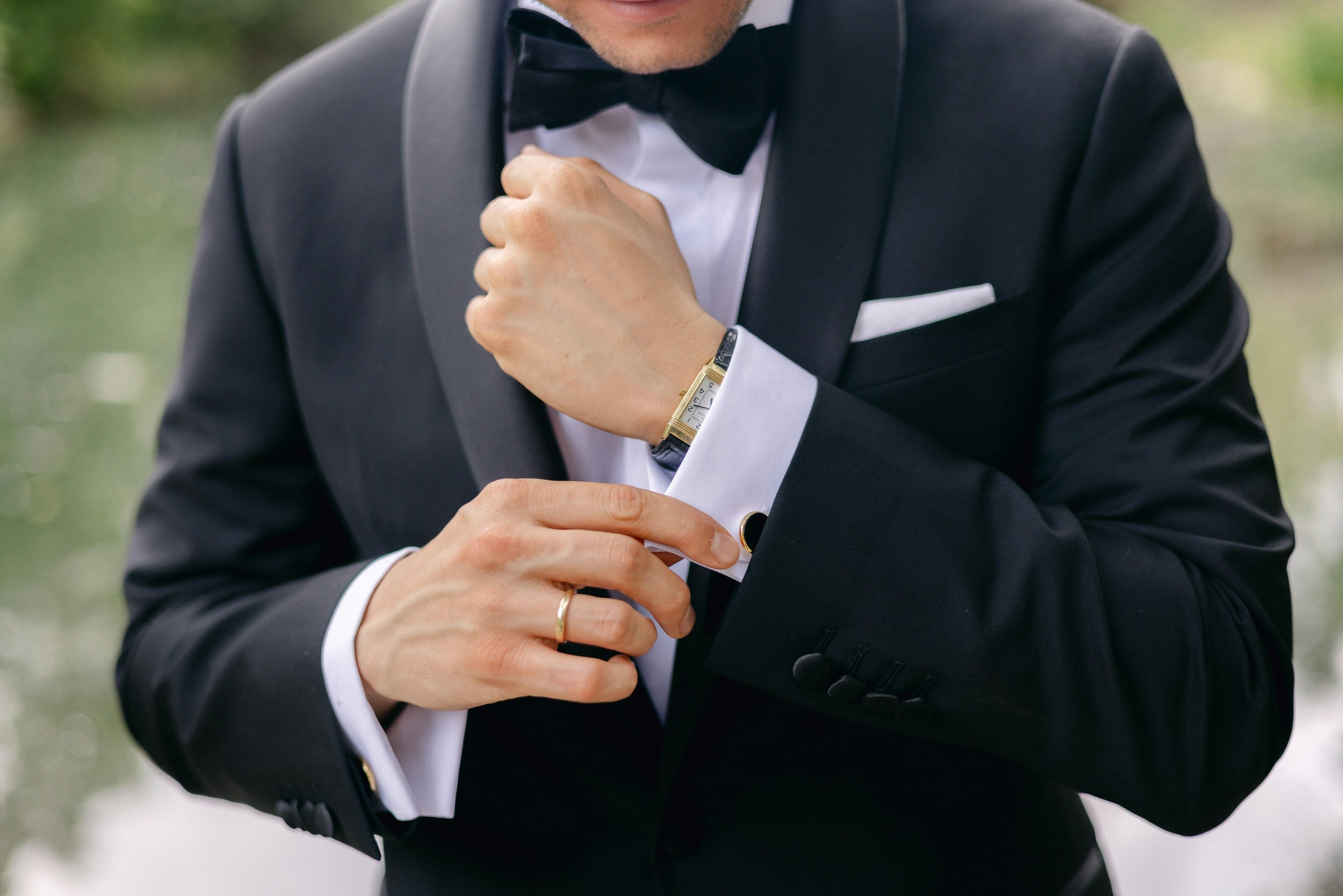 Mann im Smoking richtet konzentriert seine Uhr – steht für Präzision, Kontrolle und  bewusste Körpersprache im professionellen Verkaufsumfeld 