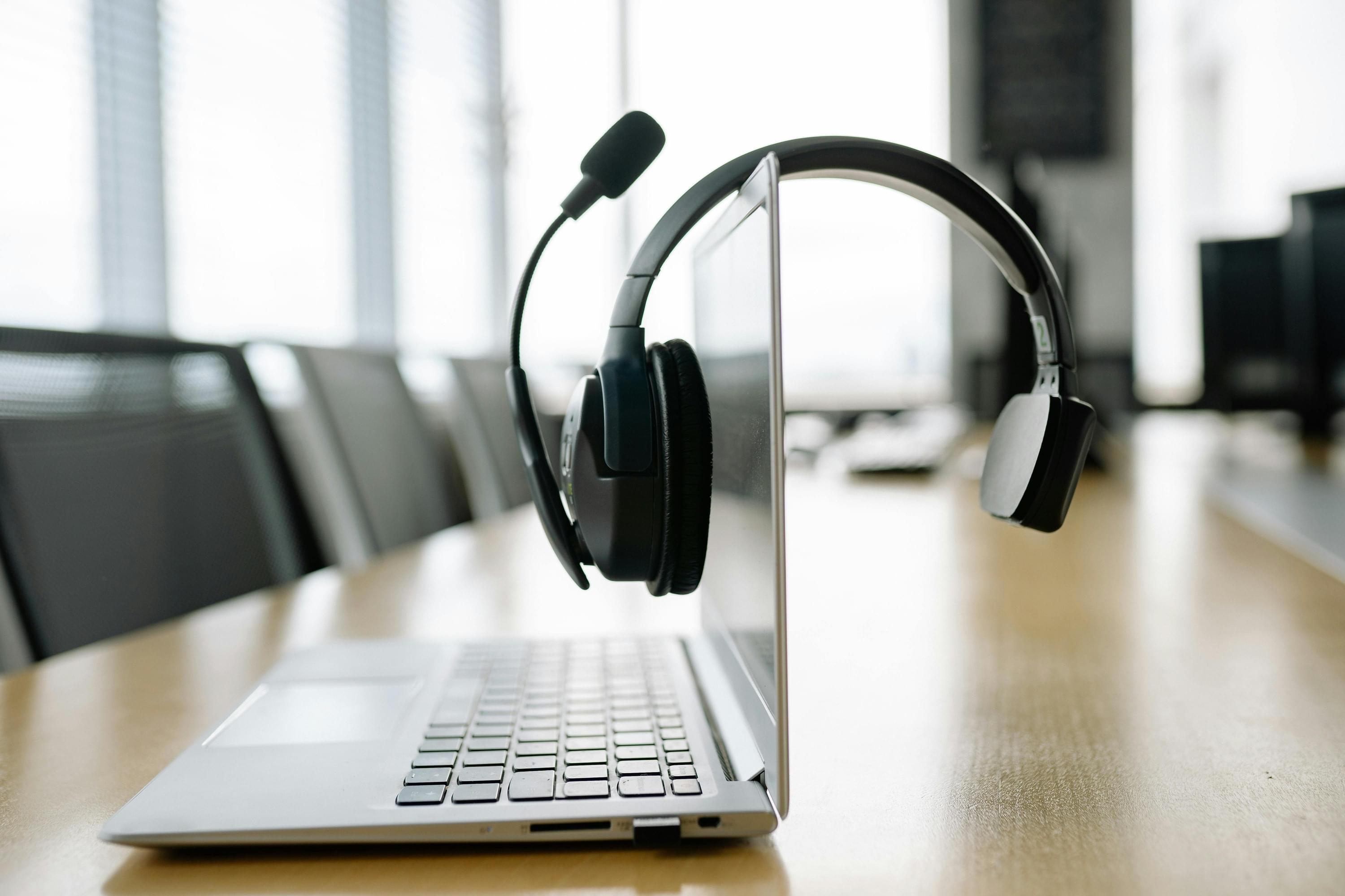  Headset hängt über einem aufgeklappten Laptop in einem modernen  Besprechungsraum – Symbolbild für digitale Kommunikation und Vertriebsgespräche.