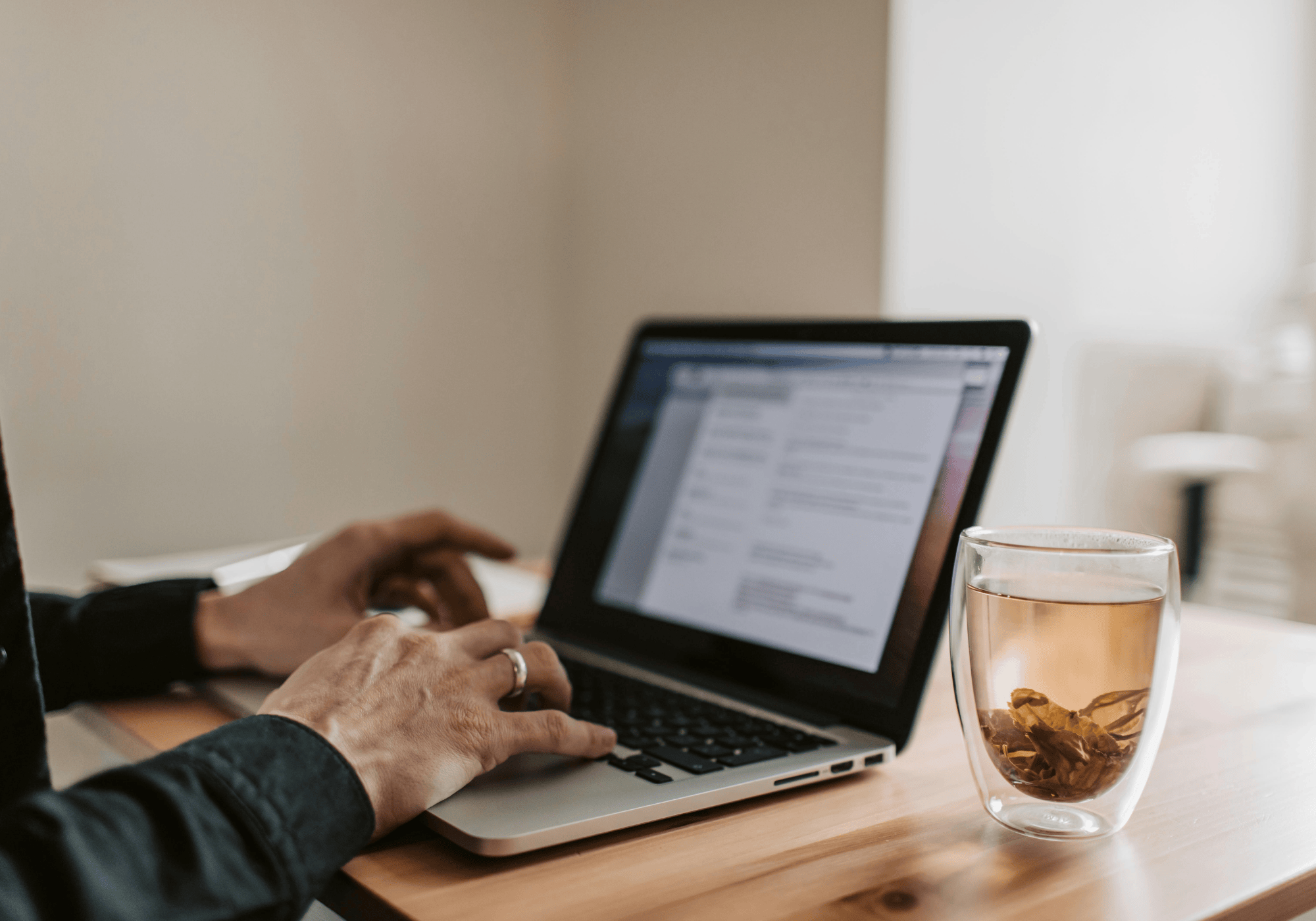 Zusatzeinkommen im Vertrieb: Person arbeitet am Laptop mit geöffnetem Dokument – daneben ein Glas Tee auf einem Holztisch, Symbol für flexibles Arbeiten